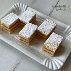 Pięć kawałków najprostszego jabłecznika, posypanych cukrem pudrem, ułożonych na białej paterze.