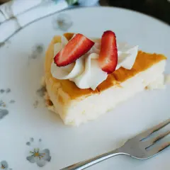 Pyszny sernik z serka wiejskiego, udekorowany bitą śmietaną i truskawkami, czeka na widelcu.