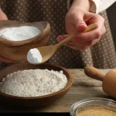 Ręce trzymają drewnianą miskę z mąką i łyżkę z sodą oczyszczoną. Szukasz co zamiast proszku do pieczenia?