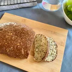 Chleb z twarogu na desce, pokrojony na kromki, obok miska z winogronami. Idealny na śniadanie.