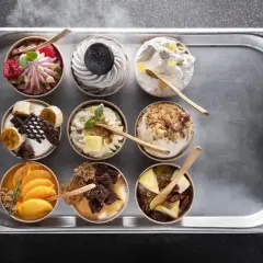 Dziewięć deserów typu parfait na tacy: malinowy, oreo, z orzechami, bananowy, pomarańczowy i inne.