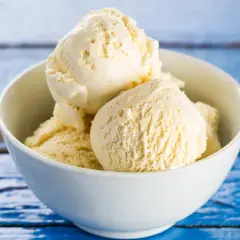 Pyszne, domowe lody śmietankowe w białej miseczce, na niebieskim, drewnianym tle. Idealne na upalne dni.
