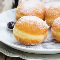 Pączki z ziemniakami Ewy Wachowicz, puszyste i obsypane cukrem pudrem, kuszą na talerzu.