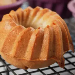 Złocista babka śmietankowa z charakterystycznymi żebrowaniami, wystudzana na kratce. W tle fioletowe foremki.