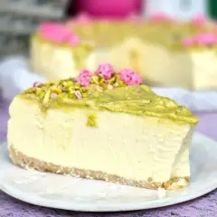 Pyszny sernik w kąpieli wodnej, udekorowany pistacjami i różowymi kwiatkami, czeka na spróbowanie.