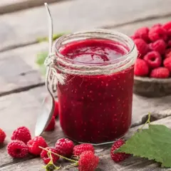 Słoik domowego sosu malinowego, obok świeże maliny i łyżeczka, gotowe do deseru.