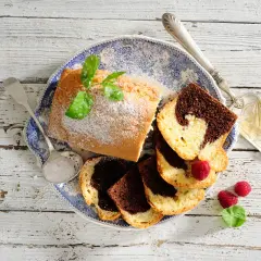 Babka piaskowa przepis babci: pyszne ciasto marmurkowe, posypane cukrem pudrem, z malinami i miętą na talerzu.