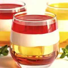 Kolorowe desery warstwowe w szklankach, idealne, gdy zastanawiasz się, jak rozpuścić żelatynę. Udekorowane listkami mięty.