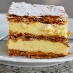 Pyszna napoleonka przepis babci: kruche ciasto przełożone kremem budyniowym, posypana cukrem pudrem.