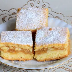 Wilgotne ciasto z jabłkami na oleju, posypane cukrem pudrem, prezentuje się apetycznie na białym talerzu.