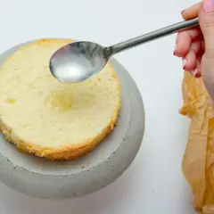 Dłoń z paznokciami pomalowanymi na różowo polewa łyżką biszkopt ponczem do tortu.