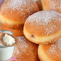 Szybkie pączki z piekarnika, oprószone cukrem pudrem, obok słoiczka z jogurtem i łyżki z jego zawartością.