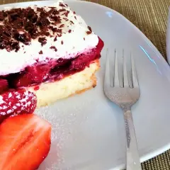 Pyszne ciasto z galaretką i truskawkami, udekorowane bitą śmietaną i czekoladą. Obok świeże truskawki i widelec.
