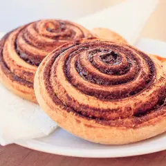 Dwa apetyczne cynamonowe ślimaki, idealne do kawy. Ich zwinięte ciasto i aromatyczny cynamon kuszą.