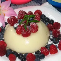 Panna cotta z malinami i borówkami, posypana cukrem pudrem. Idealny deser, który można przygotować według prostego legumina przepisu.