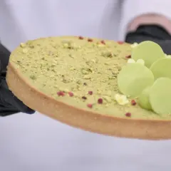 Ozdabianie mazurka pistacjowego z zielonymi czekoladowymi kuleczkami i malutkimi kwiatkami.