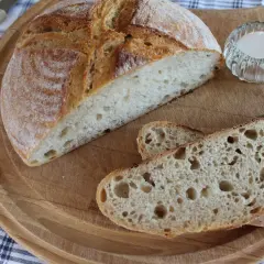 Chleb pszenno żytni na zakwasie, pokrojony na desce, z solniczką i nożem.
