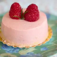 Delikatny krem malinowy z mascarpone do tortu, ozdobiony dwoma świeżymi malinami i listkiem.