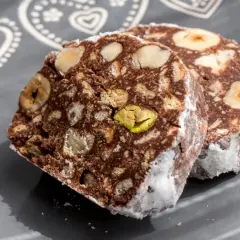 Dwa kawałki czekoladowego przysmaku z orzechami i pistacjami, przypominające blok czekoladowy przepis babci.