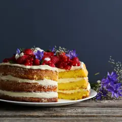 Dwa piętrowe naked cake z kremem i owocami leśnymi, ozdobione kwiatami.