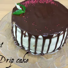 Pyszny tort drip cake z polewą czekoladową i różową posypką, ozdobiony listkami.
