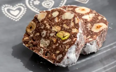 Dwa kawałki czekoladowego przysmaku z orzechami i pistacjami, przypominające blok czekoladowy przepis babci.
