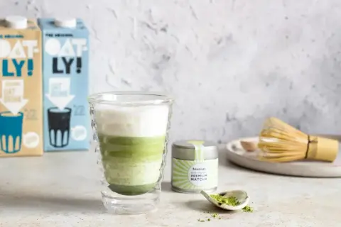 Warstwowy napój z zielonej herbaty matcha w szklance, obok puszka z napisem "PREMIUM MATCHA" i bambusowa miotełka.