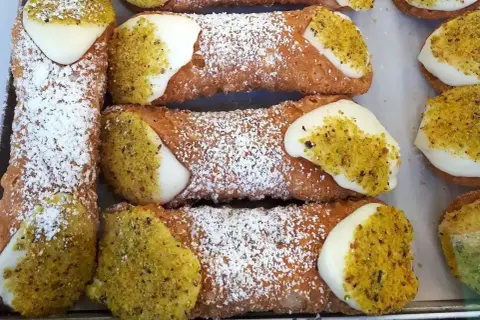 Chrupiące rurki wypełnione kremem, posypane cukrem pudrem i pistacjami. Pyszne **cannoli** czekają!