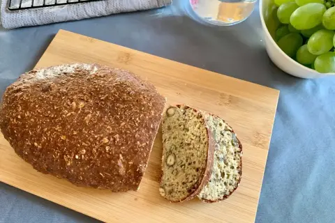 Chleb z twarogu na desce, pokrojony na kromki, obok miska z winogronami. Idealny na śniadanie.