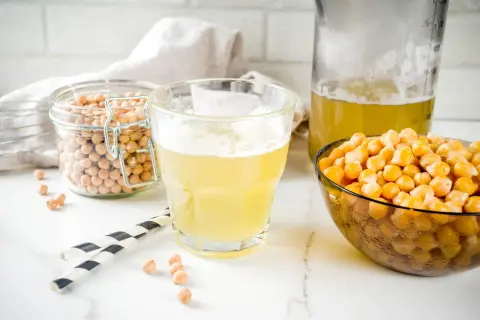 Płyn z ciecierzycy, czyli aquafaba, w szklance i dzbanku, obok miski z ziarnami. To wegański zamiennik jajek.