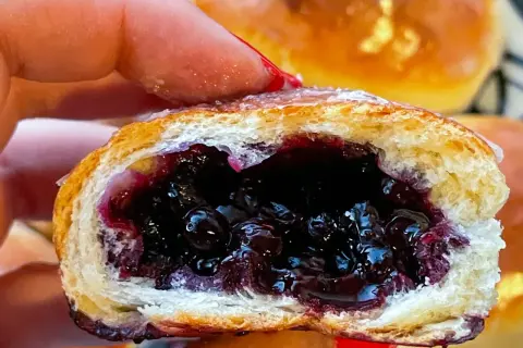 Pyszne jagodzianki z soczystym nadzieniem z jagód, trzymane w dłoni.