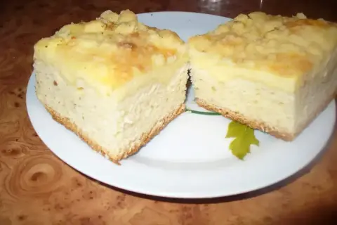 Dwa kawałki puszystego ciasta drożdżowego z serem i kruszonką, podane na białym talerzu.