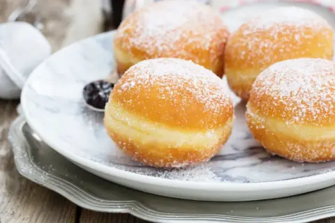 Pączki z ziemniakami Ewy Wachowicz, puszyste i obsypane cukrem pudrem, kuszą na talerzu.
