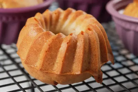 Złocista babka śmietankowa z charakterystycznymi żebrowaniami, wystudzana na kratce. W tle fioletowe foremki.