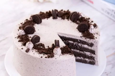 Pyszny tort z masą oreo, udekorowany pokruszonymi ciastkami i całymi ciasteczkami.