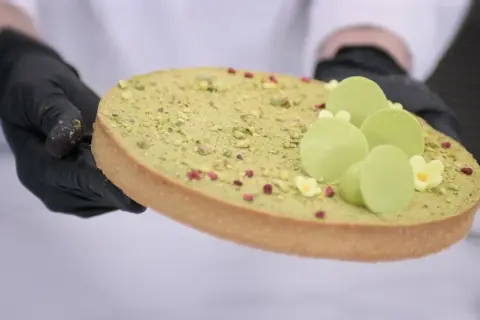 Ozdabianie mazurka pistacjowego z zielonymi czekoladowymi kuleczkami i malutkimi kwiatkami.