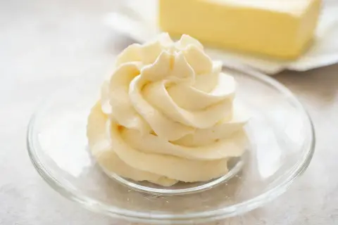 Krem patissiere w kształcie róży na talerzyku, w tle kostka masła.