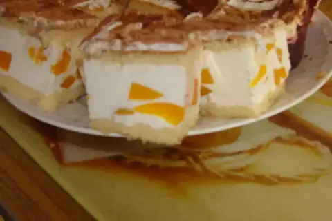 Sernik z bitą śmietaną siostry Anastazji, z kawałkami brzoskwini, posypany kakao. Pyszny deser na talerzu.