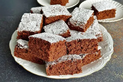 Szybkie i proste ciasto czekoladowe pokrojone w kostkę, posypane cukrem pudrem, ułożone na białym talerzu.