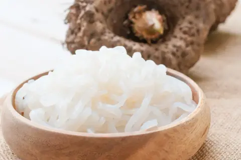 Miska pełna białego makaronu z mąki konjac, obok bulwa tej rośliny.