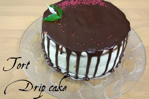 Pyszny tort drip cake z polewą czekoladową i różową posypką, ozdobiony listkami.