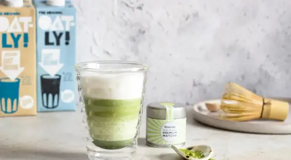 Warstwowy napój z zielonej herbaty matcha w szklance, obok puszka z napisem "PREMIUM MATCHA" i bambusowa miotełka.