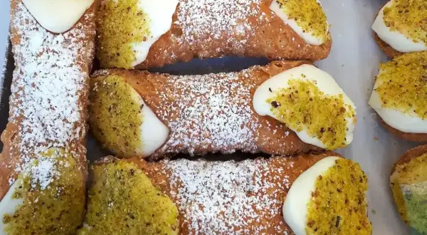 Chrupiące rurki wypełnione kremem, posypane cukrem pudrem i pistacjami. Pyszne **cannoli** czekają!