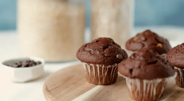 Puszyste muffinki czekoladowe, idealne na każdy przepis. W tle słoiki z cukrem i mąką.