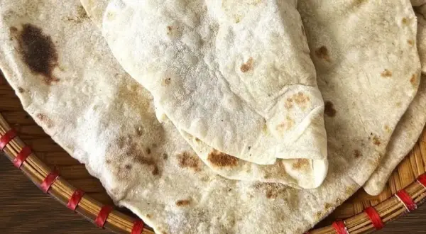 Domowy lawasz przepis. Delikatne placki z lekkimi przypaleniami, ułożone na plecionej tacce.