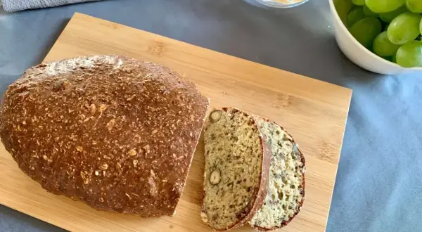 Chleb z twarogu na desce, pokrojony na kromki, obok miska z winogronami. Idealny na śniadanie.