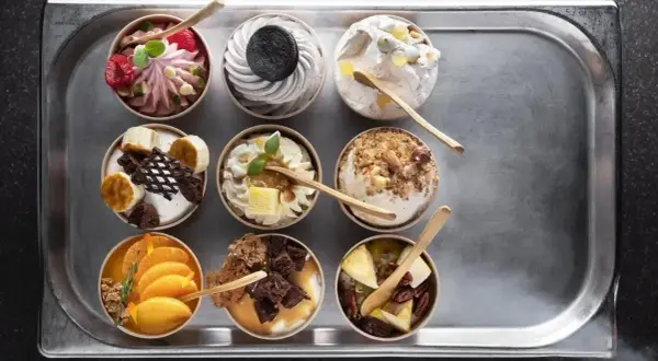Dziewięć deserów typu parfait na tacy: malinowy, oreo, z orzechami, bananowy, pomarańczowy i inne.