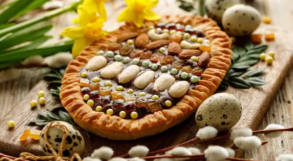 Wielkanocny mazurek ozdobiony bakaliami, orzechami i migdałami, otoczony pisankami i baziami.