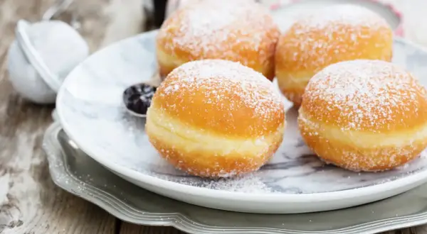 Pączki z ziemniakami Ewy Wachowicz, puszyste i obsypane cukrem pudrem, kuszą na talerzu.