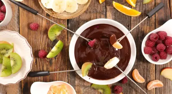Pyszne fondue czekoladowe z malinami, bananami, kiwi i mandarynkami na drewnianym stole. Idealne na deser!